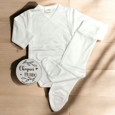 Roupa de bebé branca com pontos e calças com pés sobre chão de madeira clara, com círculo de papel ao lado