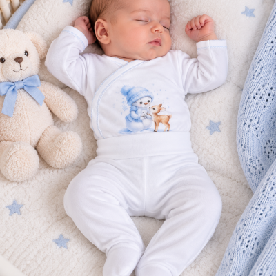 Bebé a dormir com pijama branco estampado e ursinho de peluche num berço acolchoado.