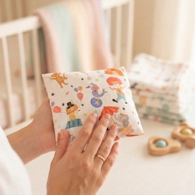 Fralda de tecido estampada com desenhos de circo nas mãos, com berço ao fundo