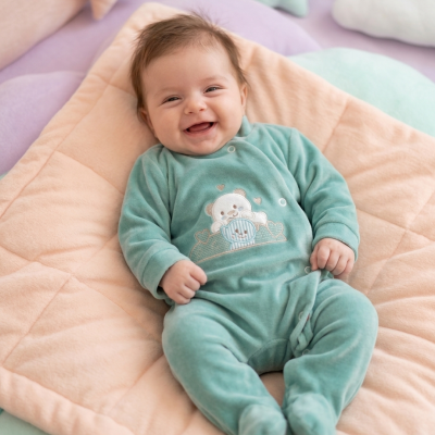 Bebé sorridente vestido com pijama verde água bordado com ursos, deitado sobre almofada cor de pêssego