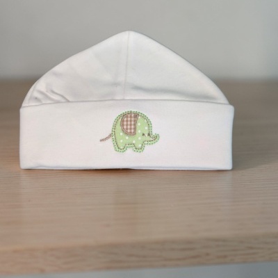Gorro branco de bebé com bordado de elefante verde sobre superfície de madeira