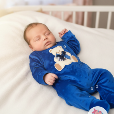 Bebé a dormir com fato de ursinho azul num berço.