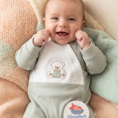Bebé de macacão verde claro com ursinho bordado sobre mantas pastéis com etiqueta redonda pirralhos