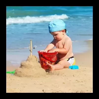 Bebé a brincar na praia com balde vermelho e castelo de areia