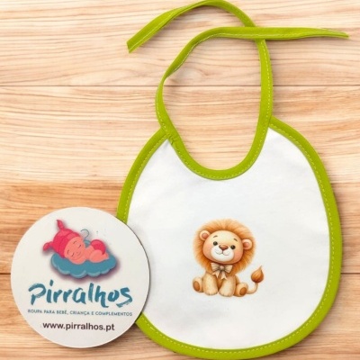 Babete branco com bordas verdes e desenho de um leão, cartão redondo com logótipo Pirralhos, fundo madeira