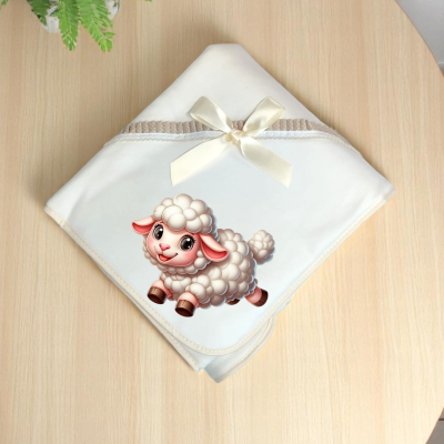 Fralda branca com ovelha estampada e laço creme numa mesa de madeira clara.