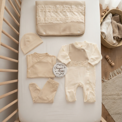 Conjunto de roupa de bebé bege e creme sobre cama de bebé de madeira clara com cesta de mantas e brinquedos ao lado