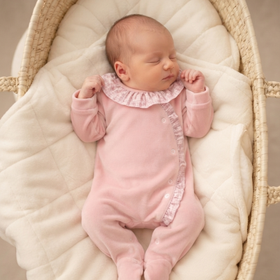 Bebé a dormir com macacão rosa num cesto de vime com almofada branca
