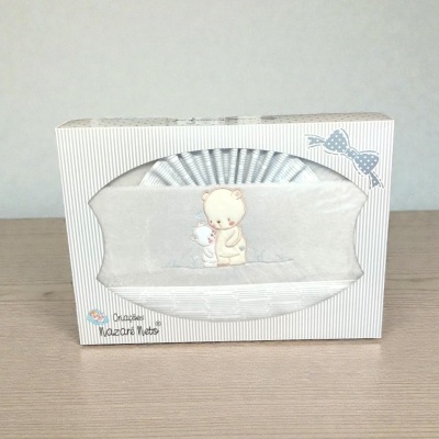 Caixa branca com riscas cinzentas contendo uma manta com bordado de ursos e laço azul na embalagem