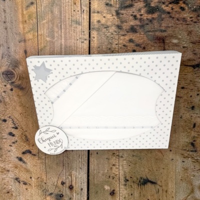 Caixa decorativa com conjunto branco de lençóis ou fraldas com bordado e fita, sobre fundo de madeira rústica