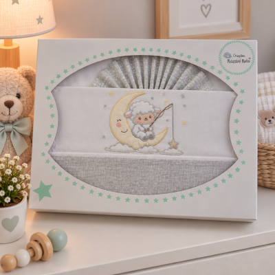 Conjunto de roupa de bebé com bordado de cordeirinho num quadro de lua, em embalagem decorada com estrelas verdes