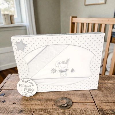 Embalagem de conjunto de roupa de bebê com desenho de coelho, timão e barco, em mesa de madeira.