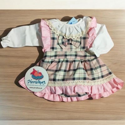 Vestido infantil às riscas com folhos rosa e blusa branca sobre madeira clara.