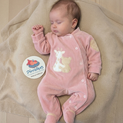 Bebé com pijama rosa de veludo e desenhos de girafa e urso, sobre manta bege