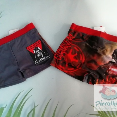 Dois boxers infantis Star Wars com cintura vermelha e estampas distintas colocados sobre superfície branca com plantas