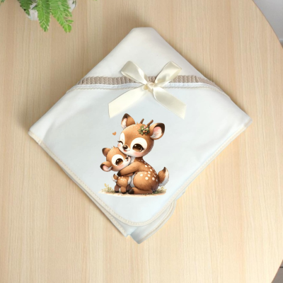 Manta branca para bebé com desenho de dois veados sobre mesa de madeira