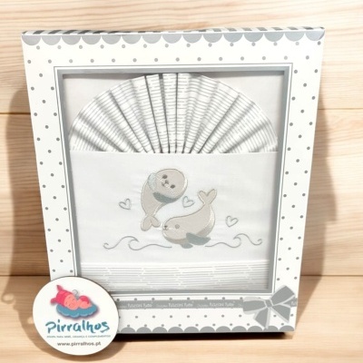 Conjunto de roupa de bebé branca com golfinhos cinza numa embalagem decorada com pontos cinza.