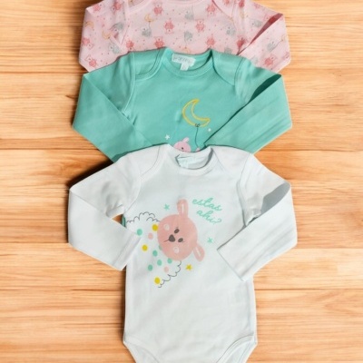 Três bodies de bebé com manga comprida em várias cores e padrões sobre fundo de madeira clara.