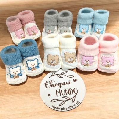 Seis pares de sapatinhos de bebé em várias cores com ursinhos bordados e cartão com texto CHEGUEI MUNDO