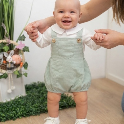 Bebé sorridente com roupa verde água e branca a ser apoiado por adulto