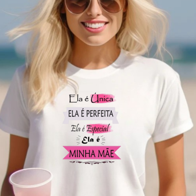 Mulher loira com t-shirt branca com texto para mãe, óculos de sol e copo plástico rosado, cenário de praia