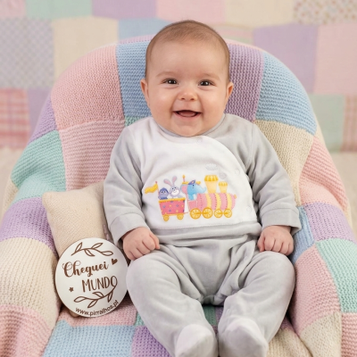 Bebé com pijama cinzento e estampagem colorida sentado em poltrona com manta de croché colorida pastel.