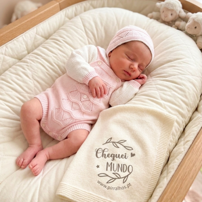 Bebé dormindo num berço acolchoado com conjunto de malha rosa e branca e mantinha creme com texto