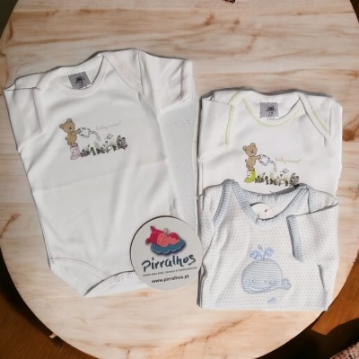 Três bodies de bebé com desenhos de animais, dois brancos e um cinza com padrão de pontos, sobre mesa de madeira clara