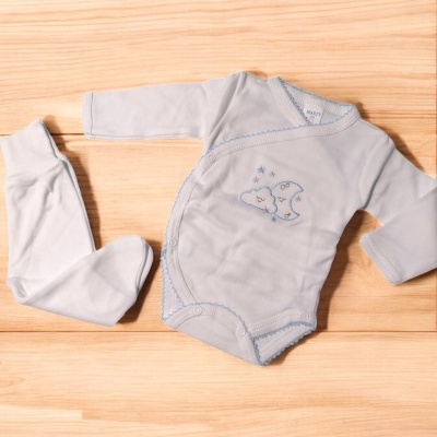 Conjunto de body e calças de bebé azul claro com bordado de lua e estrelas sobre madeira clara