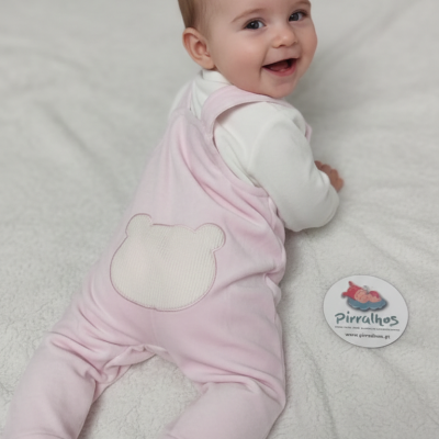 Bebé com macacão rosa e camisa branca deitado em superfície branca junto a botão com texto