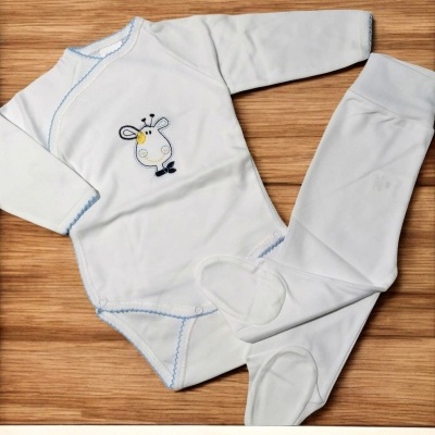 Conjunto de bebé branco com bordado de girafa e calças com pezinhos sobre madeira clara
