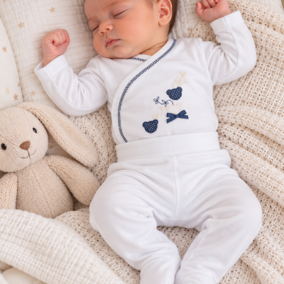 Bebé a dormir com fato branco bordado e peluche ao lado