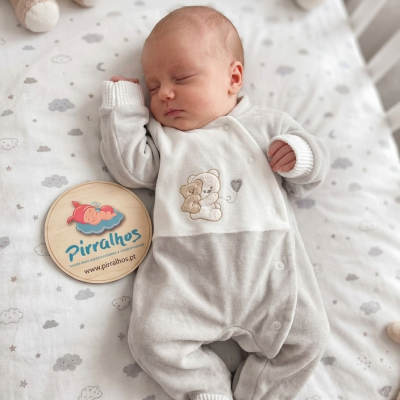 Bebé a dormir com pijama cinzento e branco e placa de madeira com logo Pirralhos