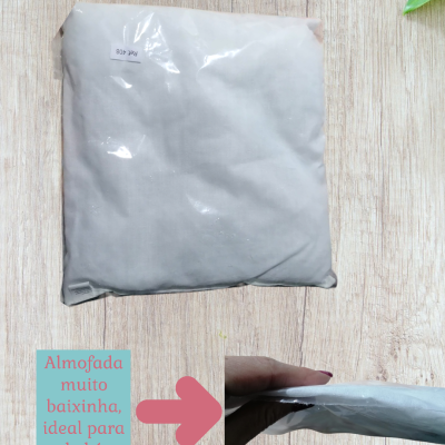 Almofada cinza clara embalada em plástico sobre madeira clara com texto descritivo em azul e seta rosa