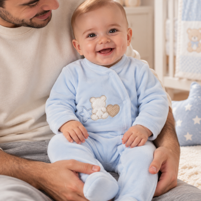 Bebé sorridente com macacão azul claro com ursinho bordado no colo do pai