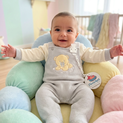 Bebé sorridente com macacão cinzento e almofadas coloridas