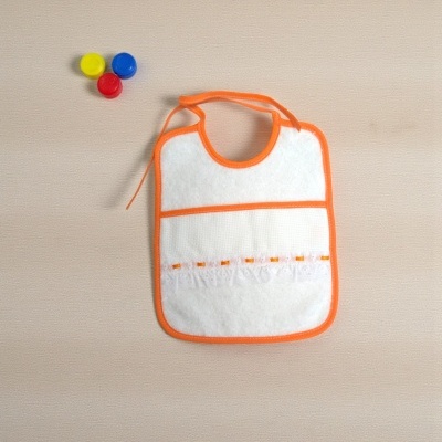 Babete branco com bordas laranja e fita decorativa, ao lado tampas amarelo, azul e vermelho