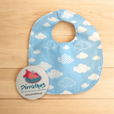 Babete azul claro com padrão de nuvens e etiqueta redonda com logótipo