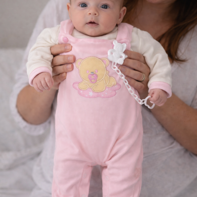 Bebé com macacão cor-de-rosa com urso bordado e chupeta branca com clipe em forma de urso