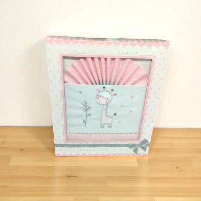 Produto têxtil para bebé com imagem de girafa dentro de caixa branca com detalhes cor-de-rosa