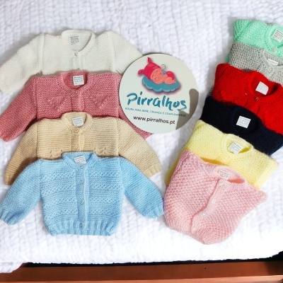 Conjunto de camisolas de malha coloridas para bebé numa cama com logotipo Pirralhos
