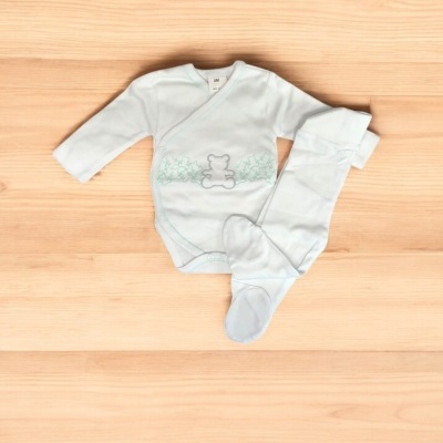 Conjunto de bebé branco com ursinhos verdes e cinzentos sobre madeira clara