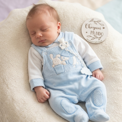 Bebé dormindo com roupa azul e branca e placa decorativa ao lado