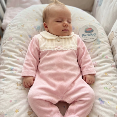 Bebé vestido com fato de corpo rosa com golinha branca a dormir numa almofada com padrão de ovelhas.