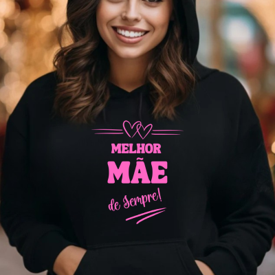 Sweatshirt preta com texto rosa 'MELHOR MÃE de Sempre!' e dois corações, numa mulher sorridente.