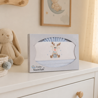 Caixa com toalha infantil bordada com rena a segurar presente numa cómoda branca com coelho de peluche ao lado