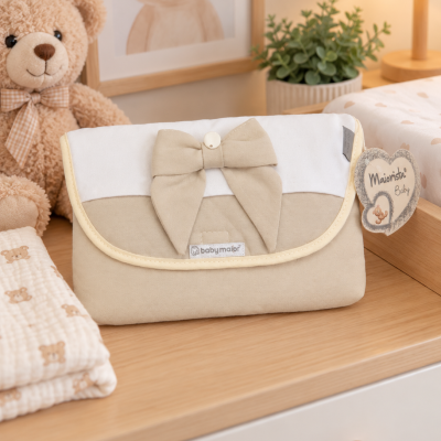 Necessaire de bebé bege e branca com laço, etiquetada baby major numa cómoda com ursinho de peluche e planta.