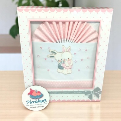 Caixa branca e rosa com babetes decorados com coelhos abraçados.