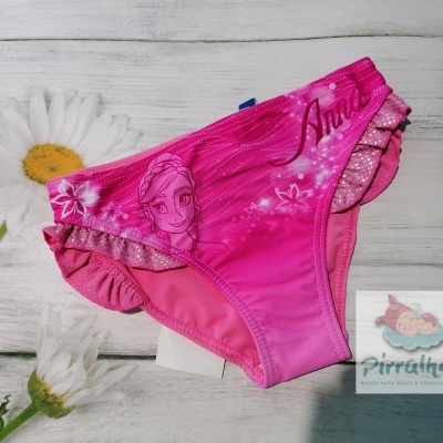 Cueca de banho infantil rosa com estampa da personagem Anna, babados e etiqueta Pirralhos sobre madeira branca com flores