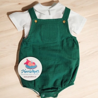 Conjunto de roupa de bebé com body branco e jardineira verde sobre superfície de madeira clara